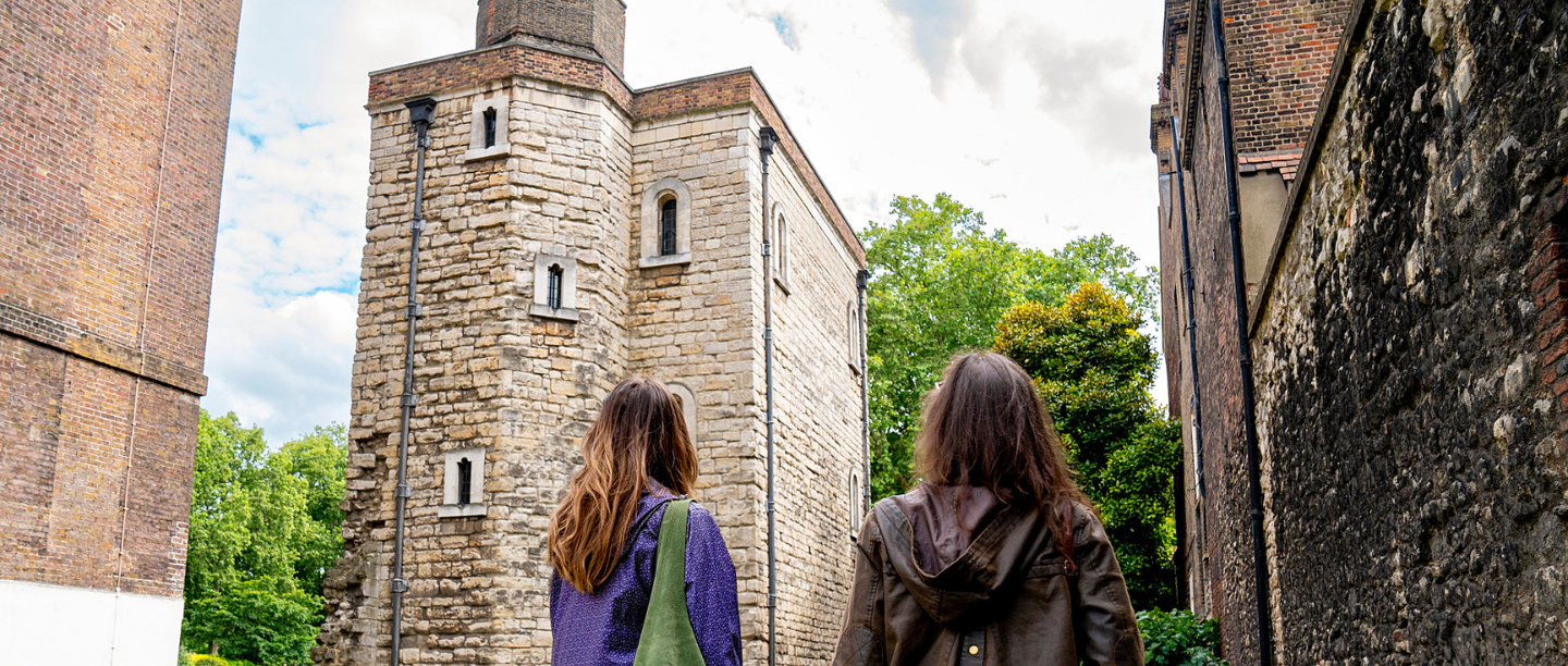 Two women walk side by side towards the stone Jewel Tower.