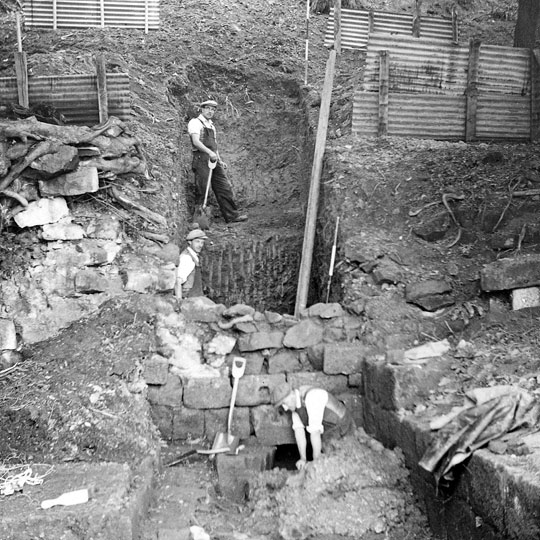 Black and white photograph of excavations at Mount Grace priory in 1957, two diggers in flat caps, waistcoats and rolled up sleeves