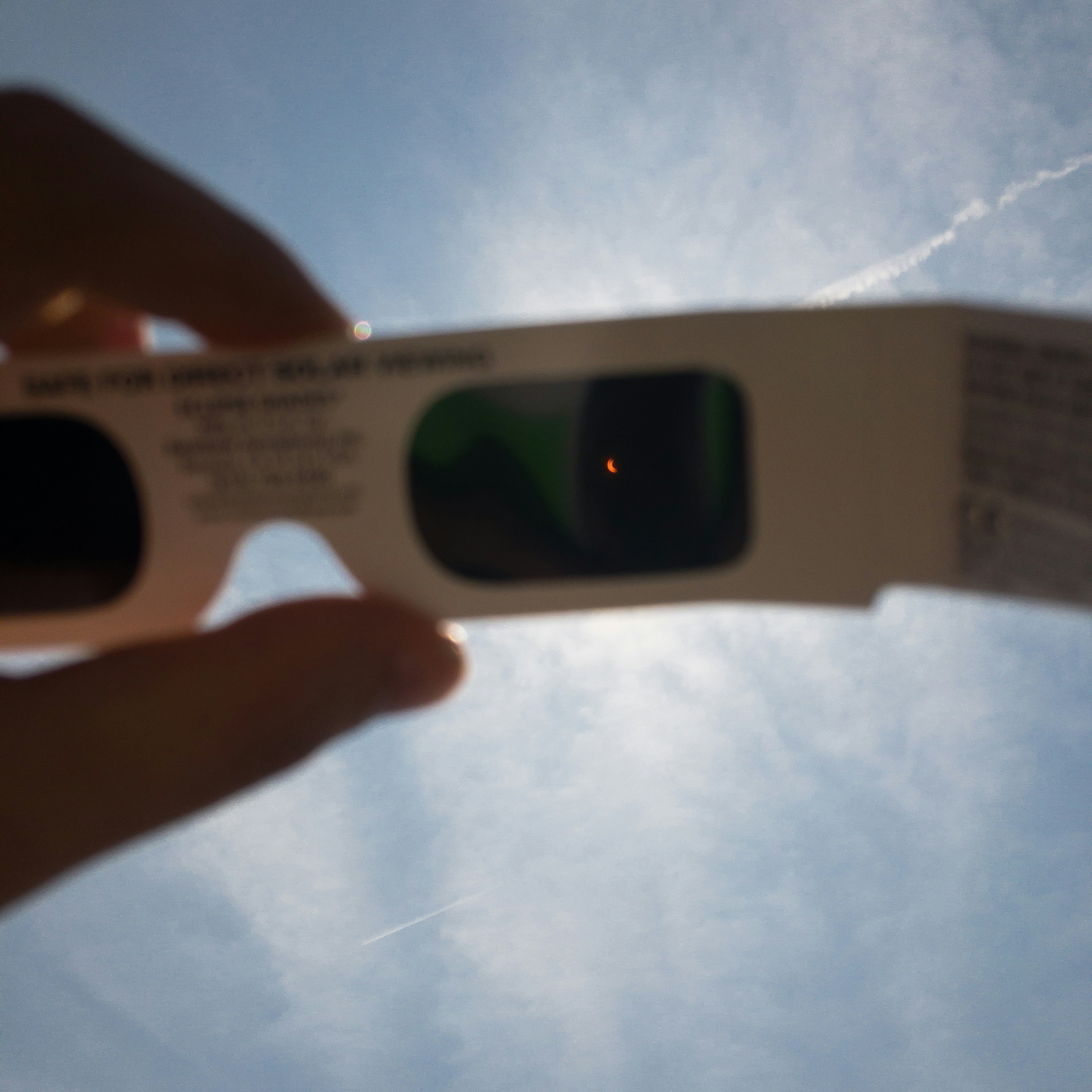 A pair of certified eclipse viewing glasses are held up to the sun during a solar eclipse.