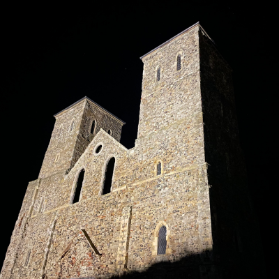 Reculver Towers at night. Two illuminated stone towers of a medieval ruin standing against a dark sky.