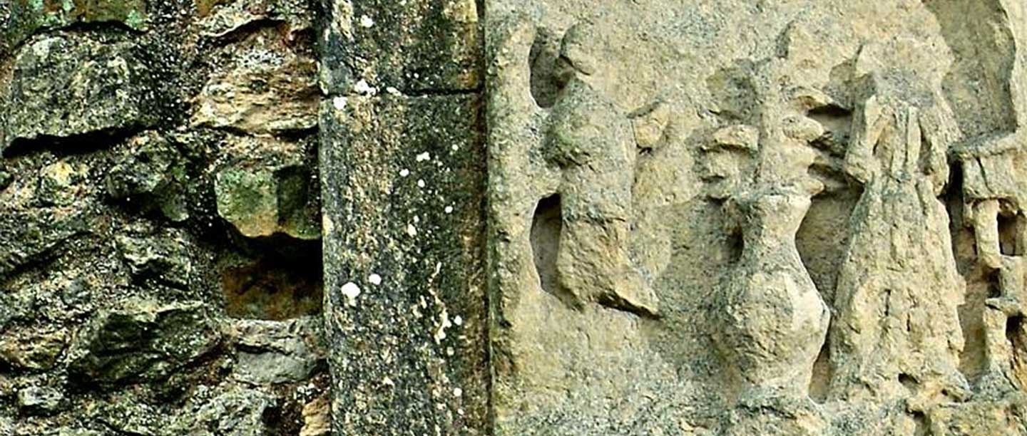 A wide image showing a close view of a very weathered stone panel set into a brick wall