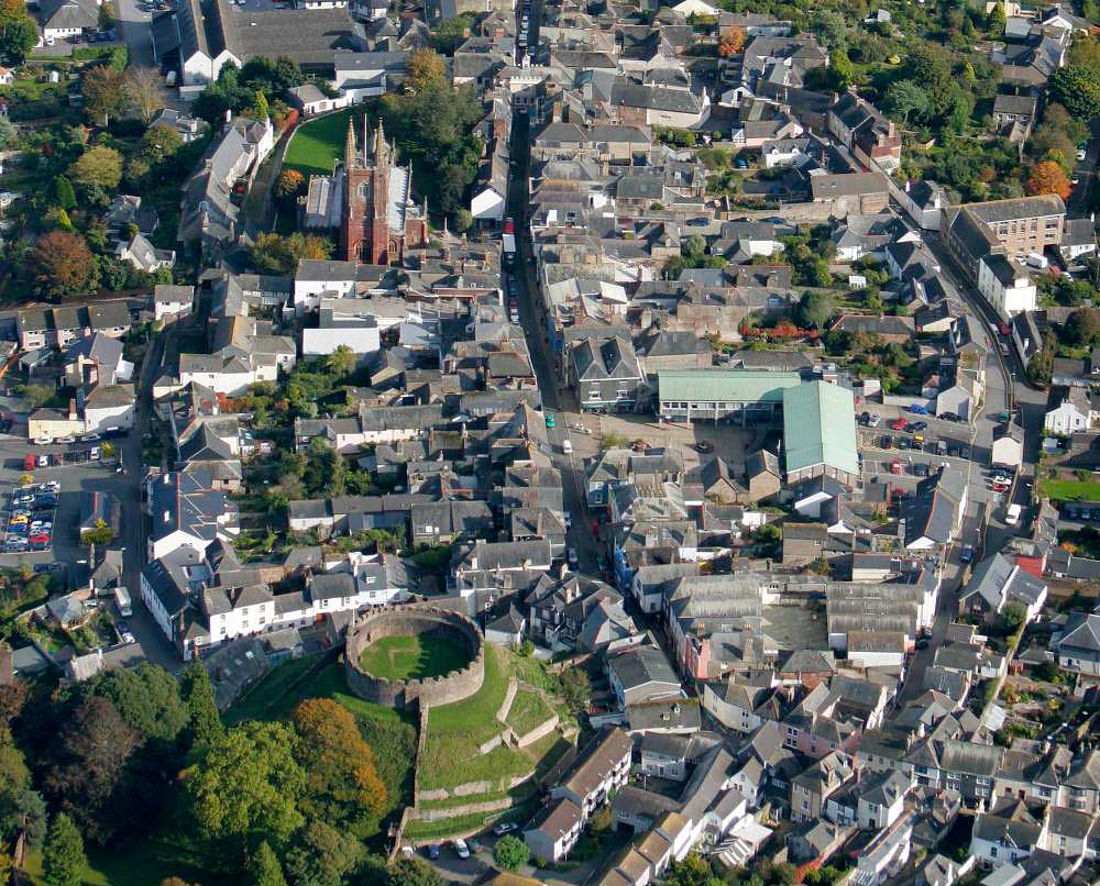 Aerial photograph looking east, showing the historic centre of Totnes, with the castle in the foreground. The curving streets to left and right of the main thoroughfare mark the boundaries of the Anglo-Saxon town, to which the Normans added the castle around 1087