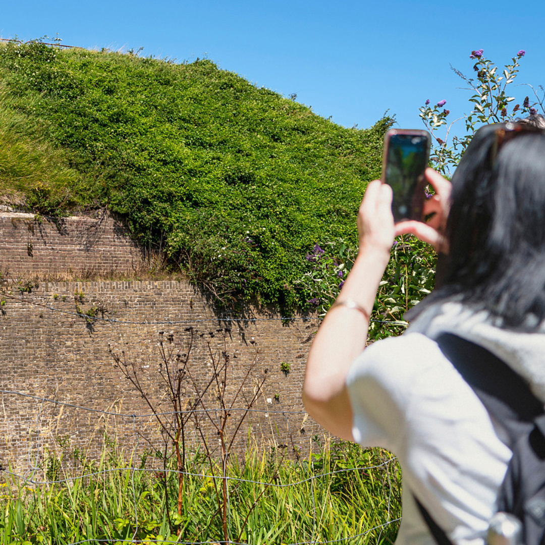 A woman holds up a smartphone to photograph a historic brick-built building.