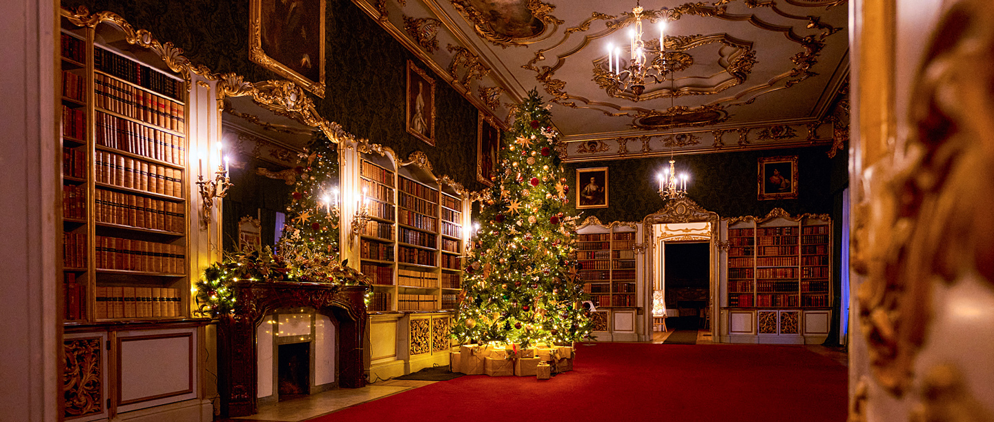 A view of a reception room at Wrest Park decorated for Christmas at night. 