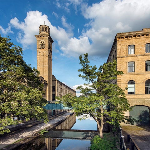 A canal runs between a mill building and a tower in Saltaire