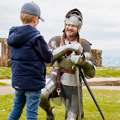 A man dressed as a knight bends on his knees to talk to a young visitor