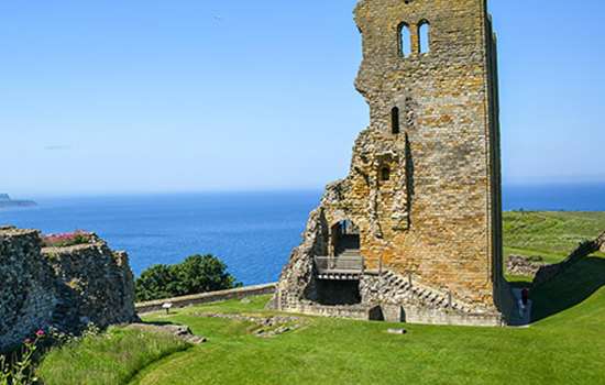 A ruined castle tower surrounded by grass with the sea in the distance on a sunny day (Scarborough Castle) A ruined castle tower surrounded by grass with the sea in the distance on a sunny day (Scarborough Castle)