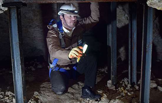 A man with a hard hat crouches in a low cave or tunnel A man with a hard hat crouches in a low cave or tunnel