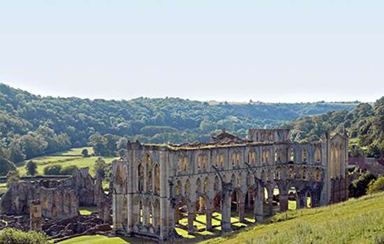 Looking down a grassy hill to the tall ruins of Rievaulx Abbey Looking down a grassy hill to the tall ruins of Rievaulx Abbey