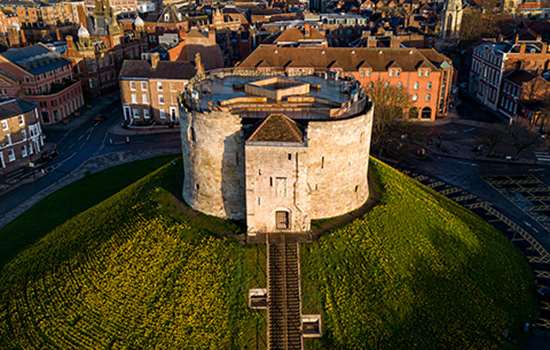 A squat tower (Clifford's Tower) sits on a large grass mound A squat tower (Clifford's Tower) sits on a large grass mound
