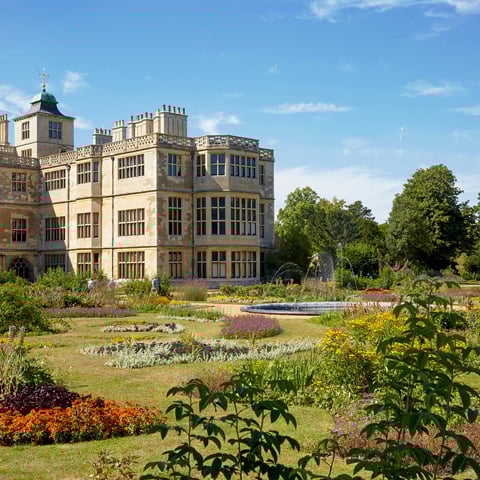 A view of the flower beds with a variety of brightly coloured flowers with Audley End House in the foreground.