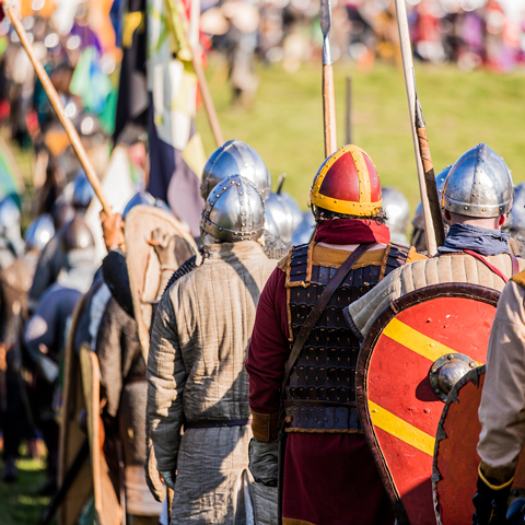 Soldier reenactors wearing armour stand in a field with thier backs turned in a field at Battle Abbey.
