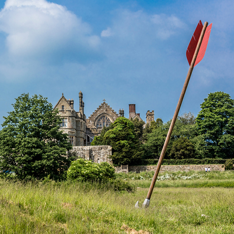 A red arrow positioned in a field, with view of Battle Abbey in the background.