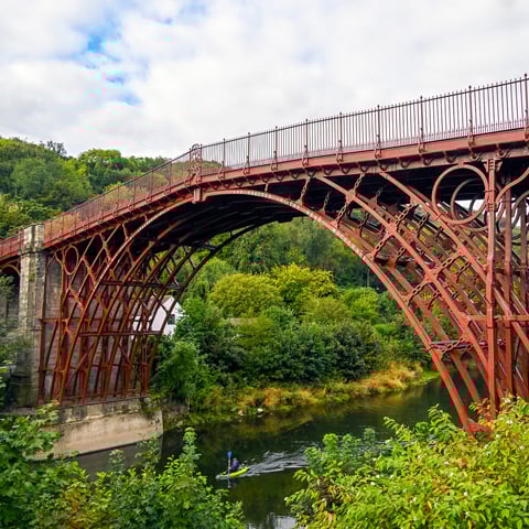 A close-up view of the Iron Bridge in Shropshire over the river. Someone is kayaking underneath the bridge's arch.