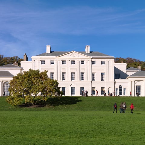 A view of the facade of Kenwood House with people walking in front of the building. 