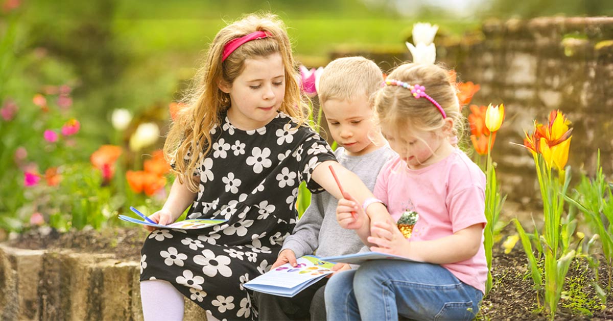 Three children sit on a wall looking at quest leaflet
