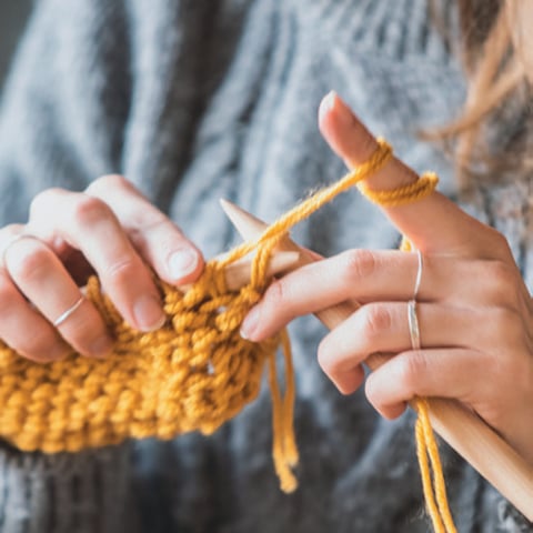 A close up view of someone knitting using a mustard coloured wool.