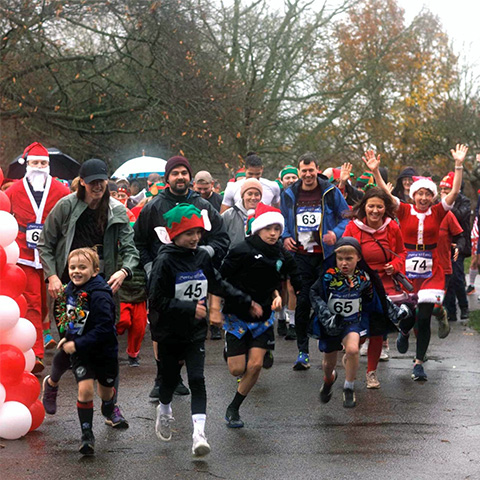 A group of runners start a race, some wearing Santa hats, on a rainy, wintry day
