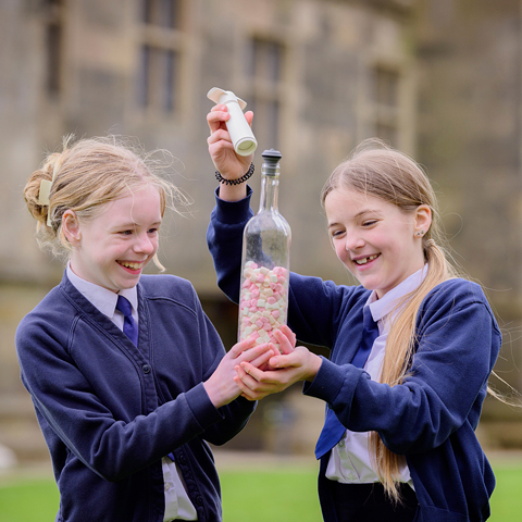 Two children in blue school uniforms hold a glass bottle filled with marshmallows at Bolsover Castle. 