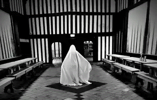 A black and white image of a figure covered in a large white sheet in a large striped timber-framed hall. A black and white image of a figure covered in a large white sheet in a large striped timber-framed hall.
