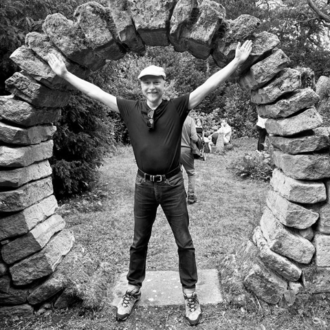 A black and white photograph of the workshop leader, Sebastian Messer, standing in a stone archway in a garden