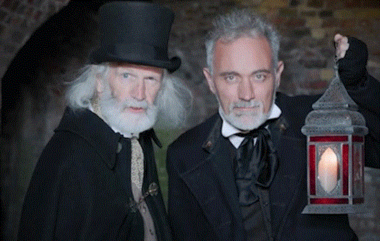 Two men dressed in Victorian style historical costumes holding lanterns in a dark setting. Two men dressed in Victorian style historical costumes holding lanterns in a dark setting.
