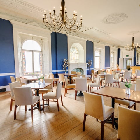 The Terrace Restaurant at Osborne which was Queen Victoria's former chapel. It has painted royal blue walls with grand chandeliers and set table and chairs.