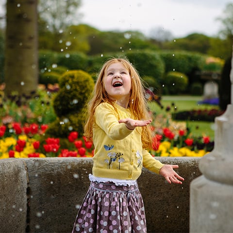 A girl laughs as she gets sprinkled by a fountain