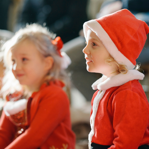 Two children wearing red Santa outfits smile looking to the left.