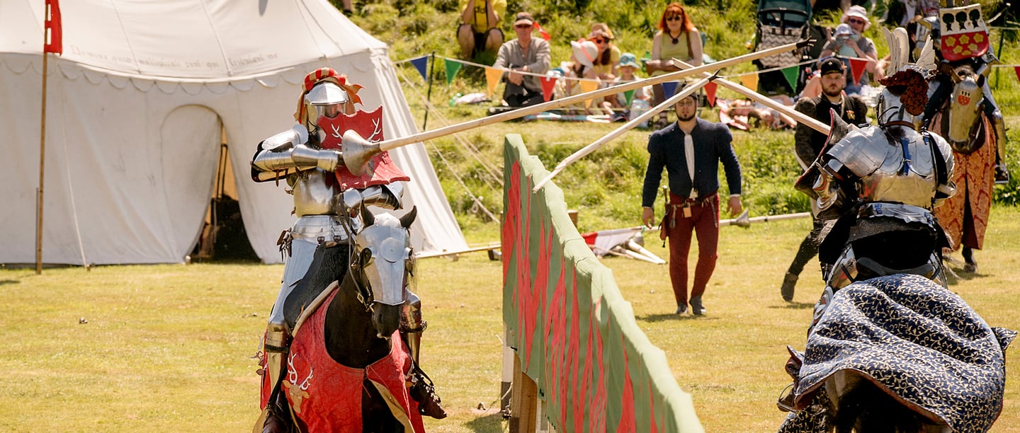 Two men on horseback re-enact a joust with spectators watching.