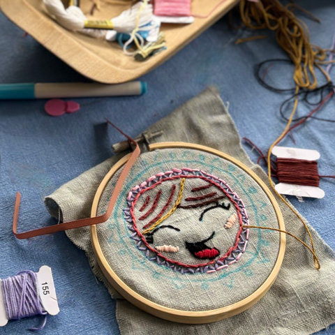 An embroidery hoop with needles and threads laid out next to it.