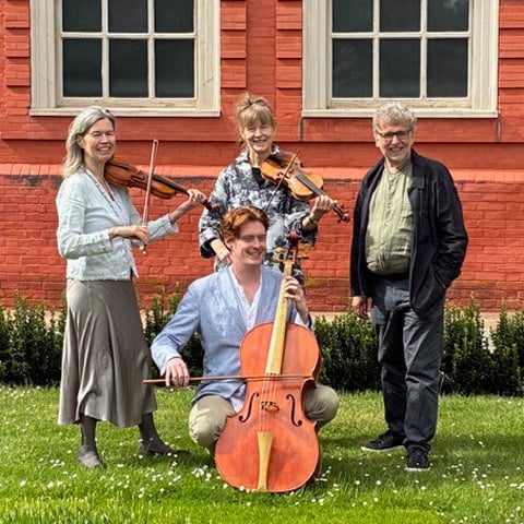 A string band smiling while holding their instruments, including violins and a cello.