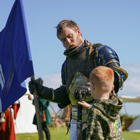 A child looks up at a man wearing Knights armour. 