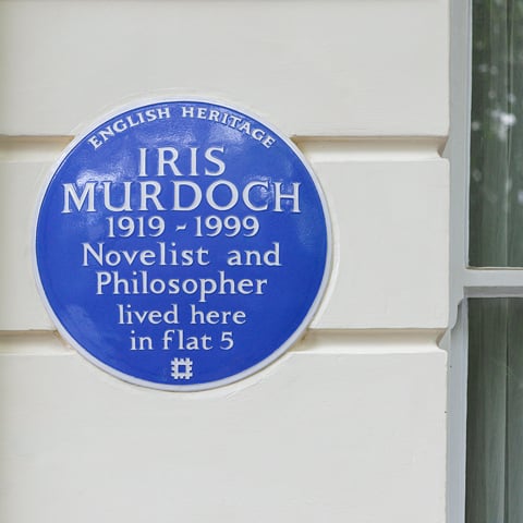 A close-up of an English Heritage Blue Plaque commemorating Idris Murdoch on a white building.