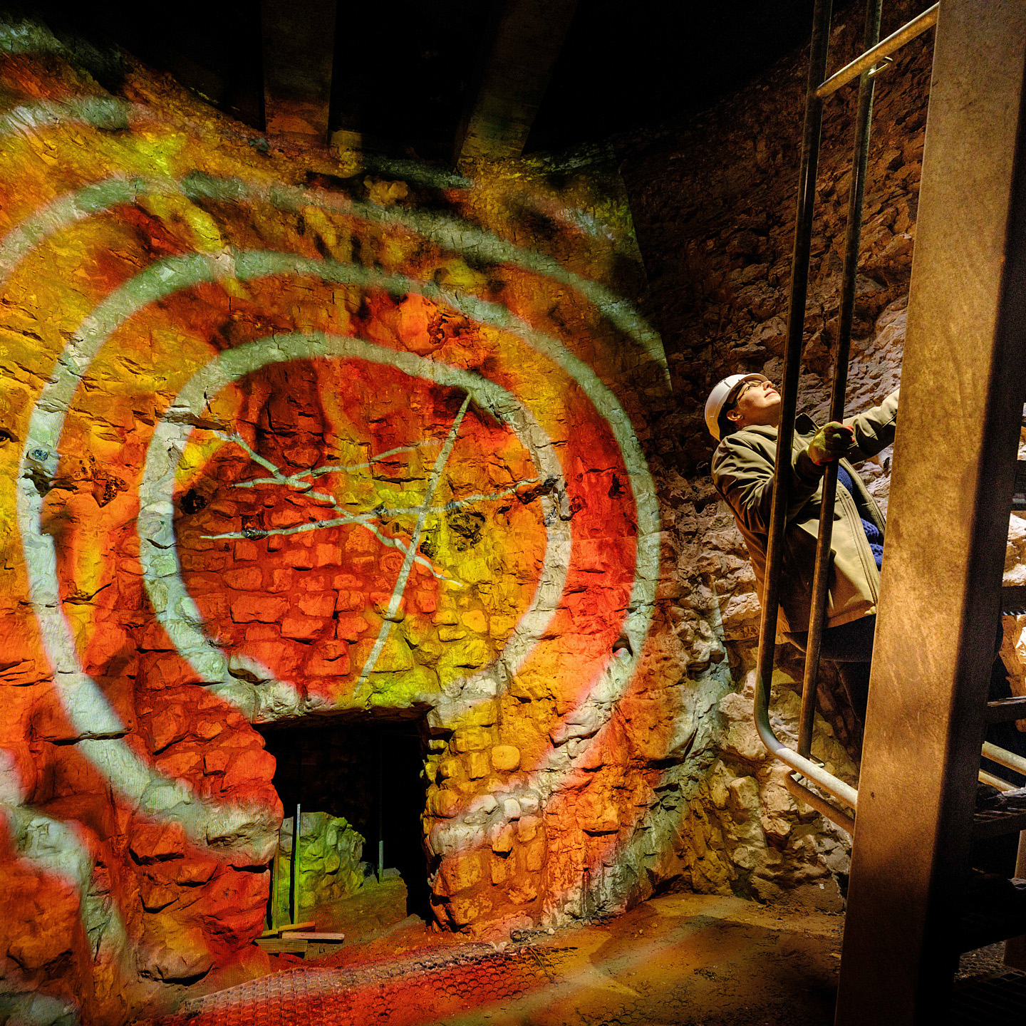 A person in a hard hat climbs a ladder in a mine at Grimes Graves.