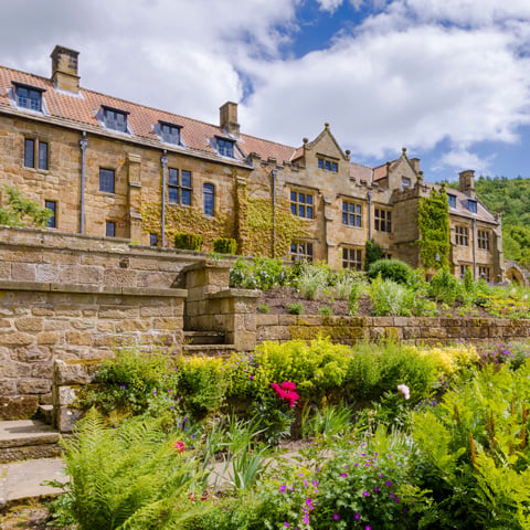 An exterior view of the stone building at Mount Grace Priory from the blooming gardens.