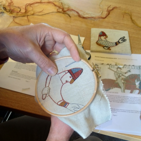 A close-up of someone doing embroidery using a fabric hoop with a Bayeux Tapestry inspired design.