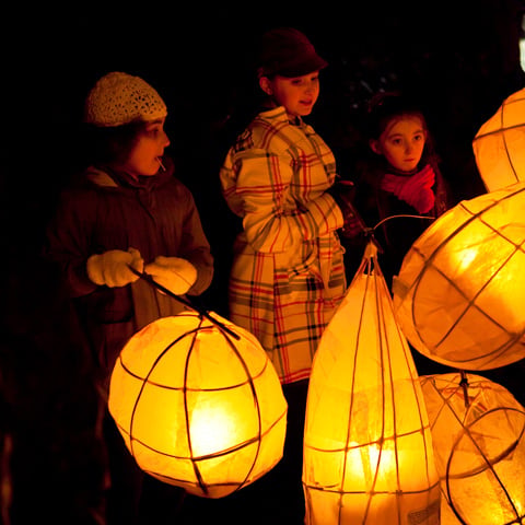Three children hold lit paper lanterns at night.