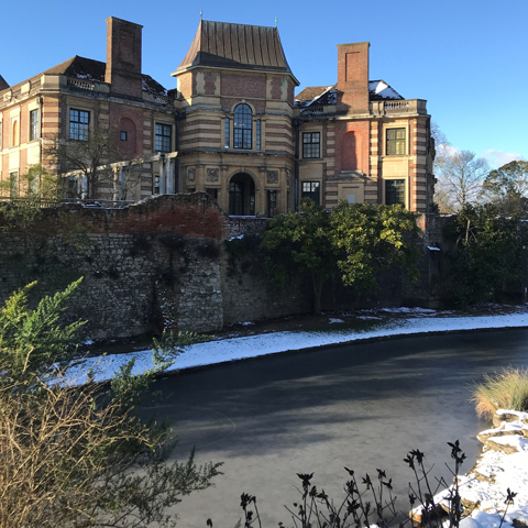 A view of Eltham Palace in the snow with the river frozen over.