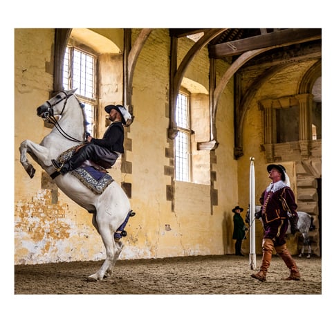 Two reencators in 17th century style clothing. One is on a horse, and one stands next to them.