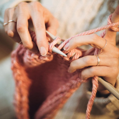 A close-up photo of someone knitting using a light pink coloured wool.