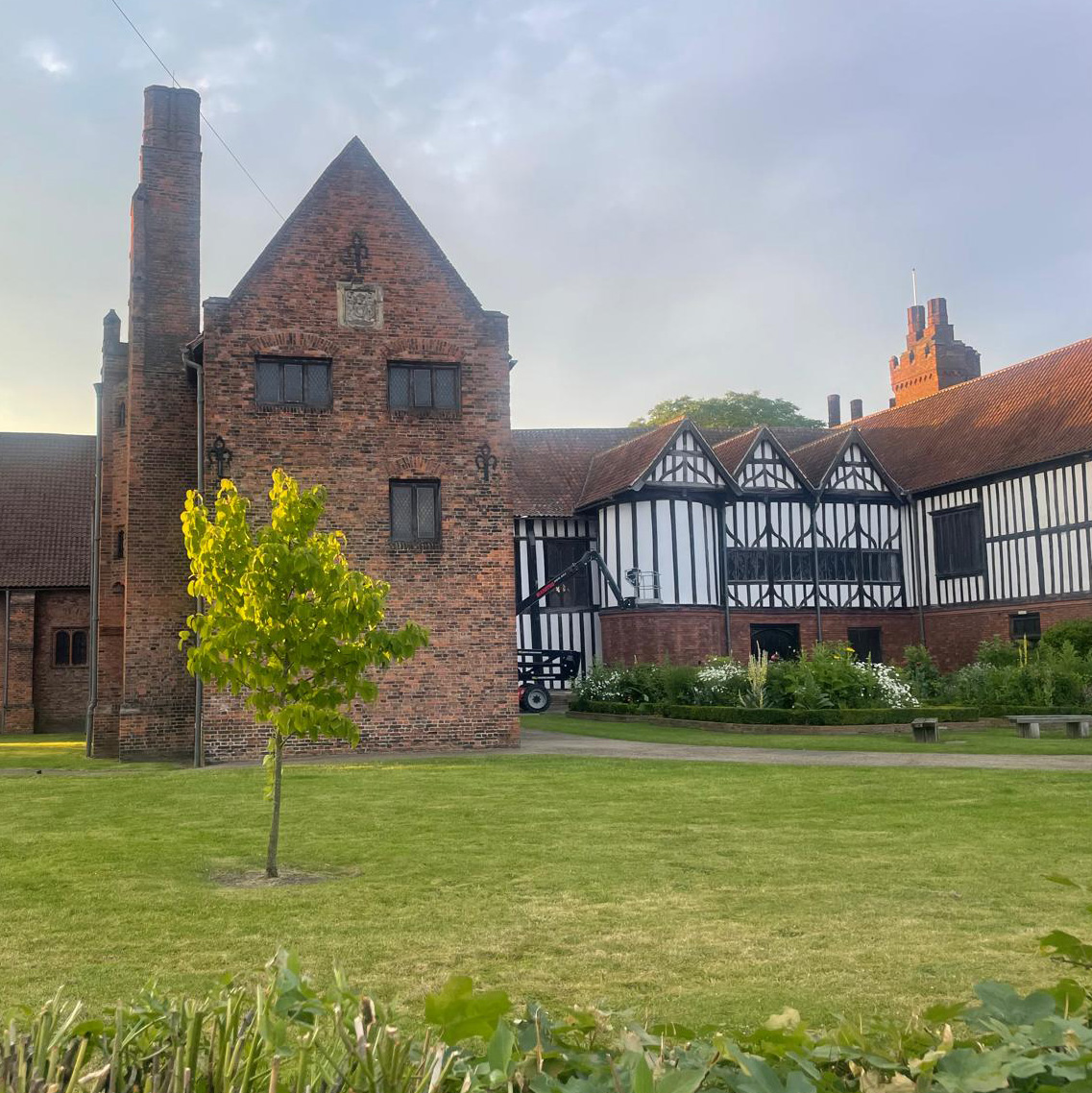 A view of the exterior of Gainsborough Old Hall and gardens underneath a sunny blue sky.