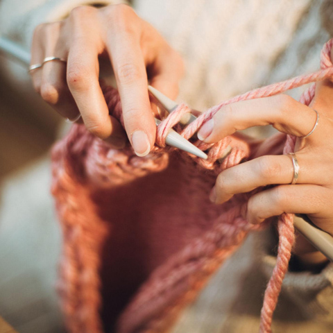 A close-up of someone knitting using pink wool.