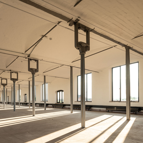 A view of an interior open space with large supporting metal beams and large windows at Shrewsbury Flaxmill Maltings..