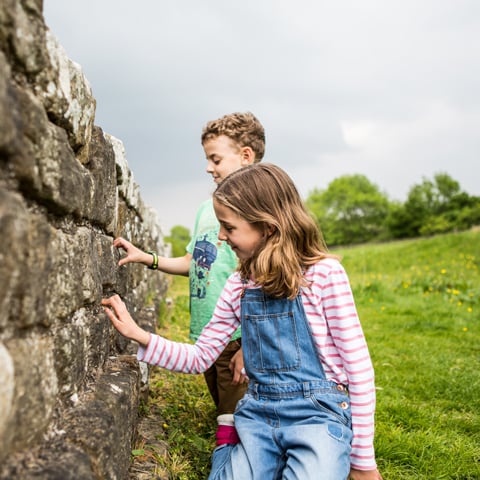 Two young children touch the Roman stone wall at Housesteads Roman Fort.