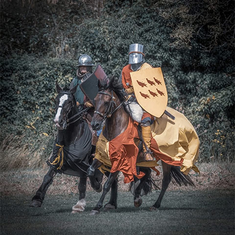 Two re-enactors dressed as knights ride two horses