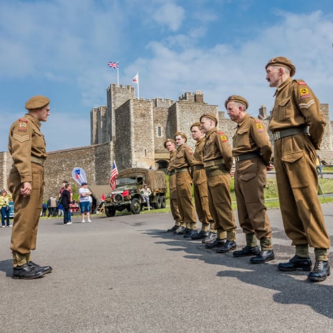 A group of WW2 soldier reenactors standing to attention with Dover Castle in the background.