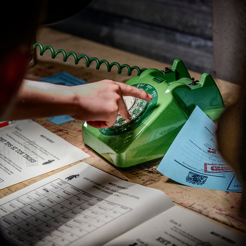 A close-up of someone operating an old fashioned green landline phone with paperwork with codes written on them.