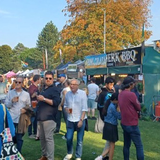 A food and drink festival with people gathered on a lawn and food stalls are in the background.