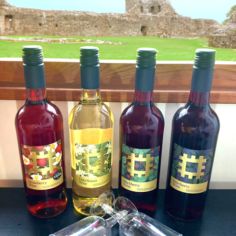 Four bottles of English Heritage wine positioned on a worktop with view of Pevensey Castle through the window in the background.